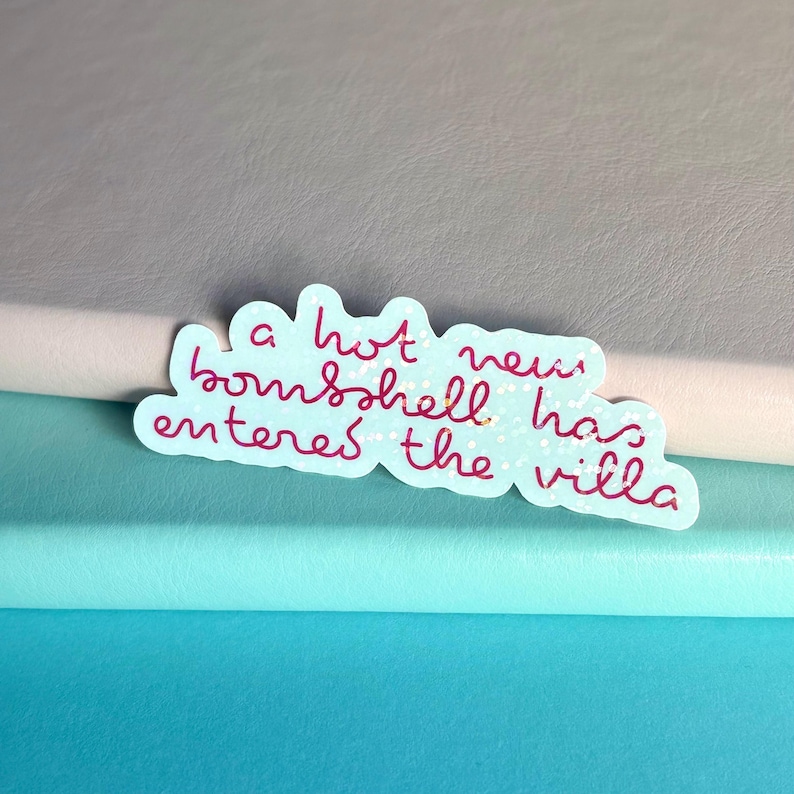 May include: A light blue sticker with the text "a hot new bombshell has entered the villa" in pink cursive. The sticker has a cloud-like shape and small white polka dots.