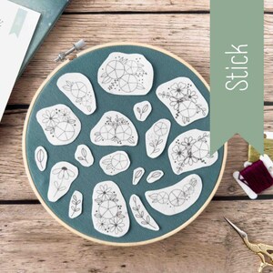 May include: A set of 16 embroidery patterns featuring floral designs with a circle in the center. The patterns are printed on white fabric and are arranged in a circle on a teal blue background. The fabric is in a wooden embroidery hoop.