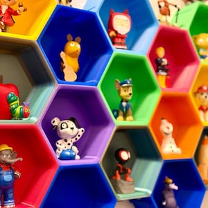 Könnte beinhalten: Bunte, wabenförmige Regaleinheit mit verschiedenen Figuren. Zu den Figuren gehören ein roter Apfel, eine Raupe, ein Dalmatiner, ein Zeichentrick-Elefant und Figuren von Paw Patrol. Die Regale sind in leuchtenden Farben lackiert.