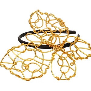 May include: A gold wire headband with a butterfly design. The headband is made of thin wire that is twisted and shaped into a butterfly. The butterfly has two wings and a body. The headband is black and has a simple design.