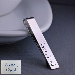 Może przedstawiać: Srebrny klips do krawata z grawerem "Love Dad" na przodzie.