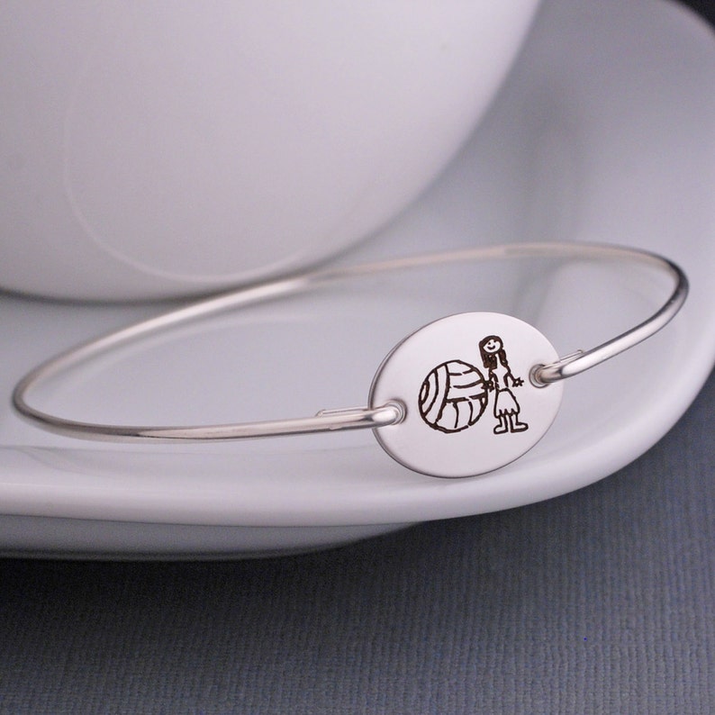 A oval shaped stainless steel disc is engraved with the art work of your choice.  The band is sterling silver and is hand formed into a bracelet.
