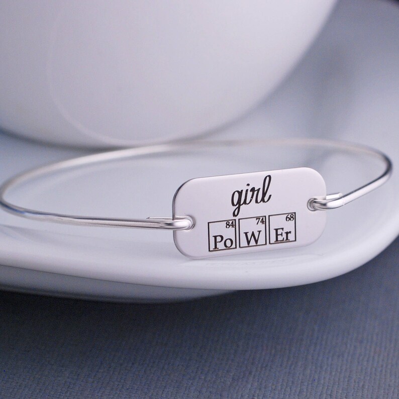 May include: Silver bangle bracelet with a rectangular tag that reads "girl" and features the chemical symbols for Polonium, Tungsten, and Erbium, with their atomic numbers.