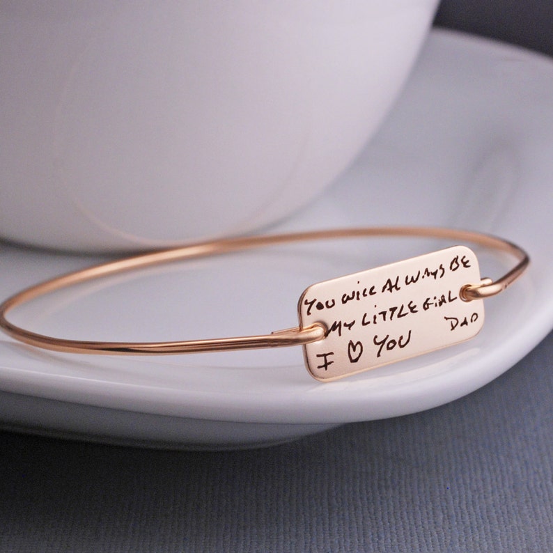 gold bangle bracelet with handwritten message engraved.  The disc is rectangle in shape and measures approximately 1 inch wide by 1/2 inch tall.