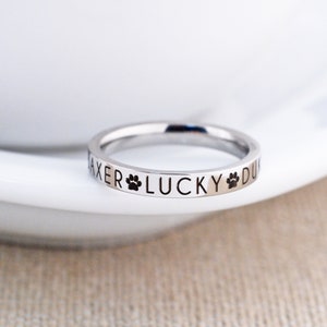 May include: A silver ring with the words "AXER LUCKY DU" engraved around the band. Two paw prints are engraved on either side of the word "LUCKY".