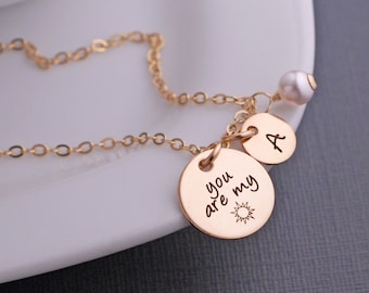 May include: Gold necklace with a small pearl charm, a charm with the letter "A" and a charm with the words "you are my" and a sun graphic.