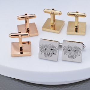 May include: A set of four cufflinks. Two are silver with a dog's face engraved on them. The other two are gold and have a simple design.