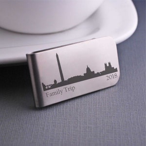 K&ouml;nnte beinhalten: Silberner Geldclip mit einer Silhouette der Skyline von Washington D.C., einschlie&szlig;lich des Washington Monuments und des Kapitols. Der Text "Family Trip 2018" ist unterhalb der Skyline graviert.