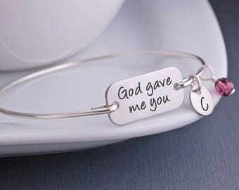 May include: Silver bangle bracelet with a charm that reads "God gave me you" and a small charm with the letter "C" and a purple crystal.