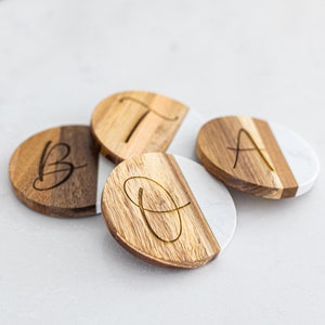 May include: Four round wooden coasters with a white marble top. Each coaster has a different letter, A, B, D, and T, engraved on the wood.