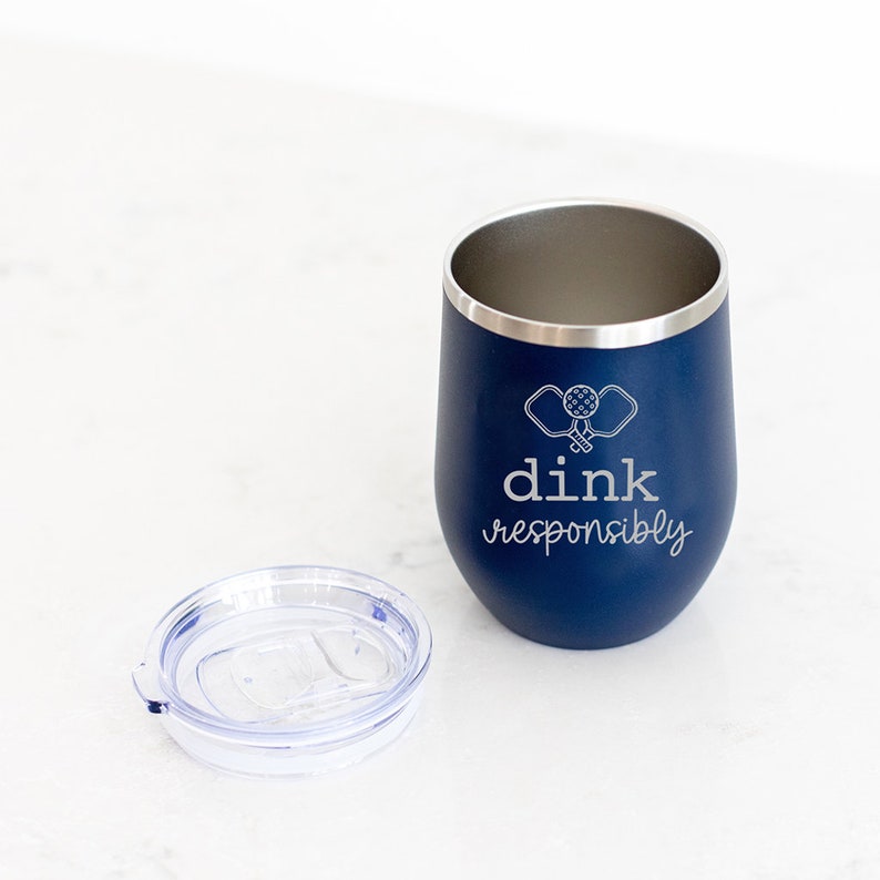 May include: A blue stainless steel tumbler with a white lid and a white graphic of two pickleball paddles and the text "dink responsibly".