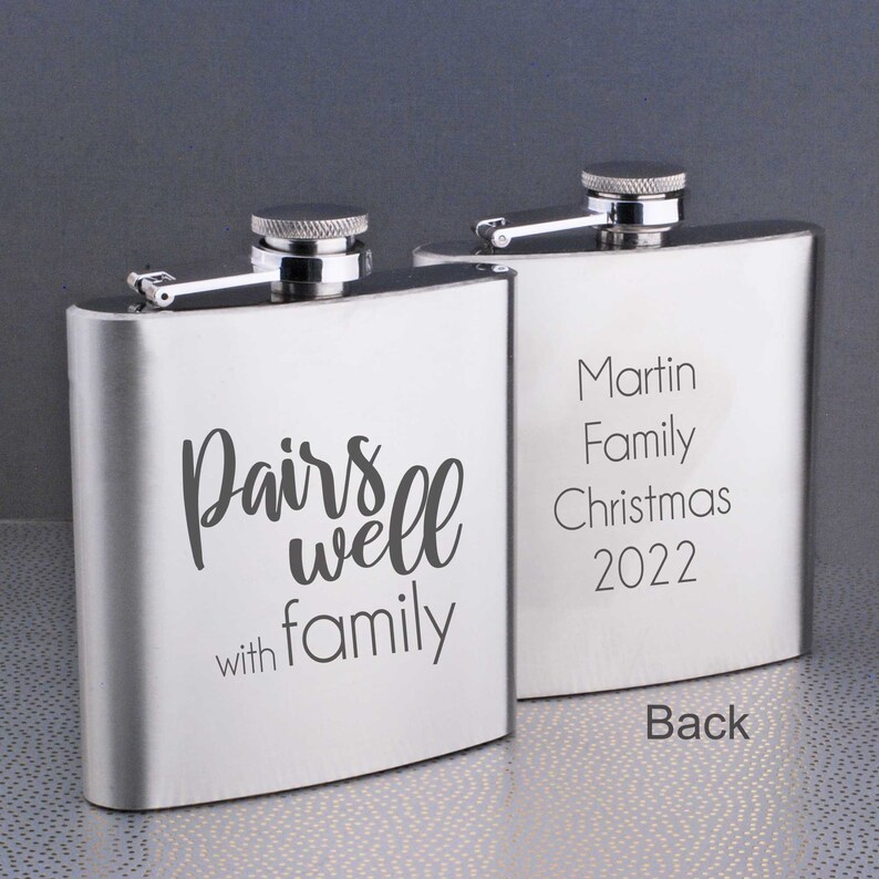 Może przedstawiać: Dwie srebrne karafki z grawerowanym tekstem. Jedna karafka m&oacute;wi "Pairs well with family". Druga karafka m&oacute;wi "Martin Family Christmas 2022".