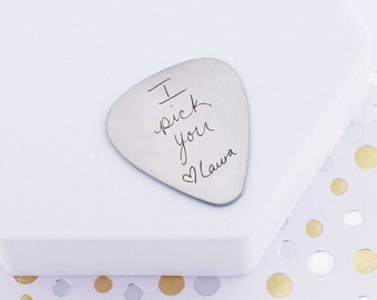 May include: A silver guitar pick with the inscription "I pick you" and a heart with the name "Laura" engraved on it.