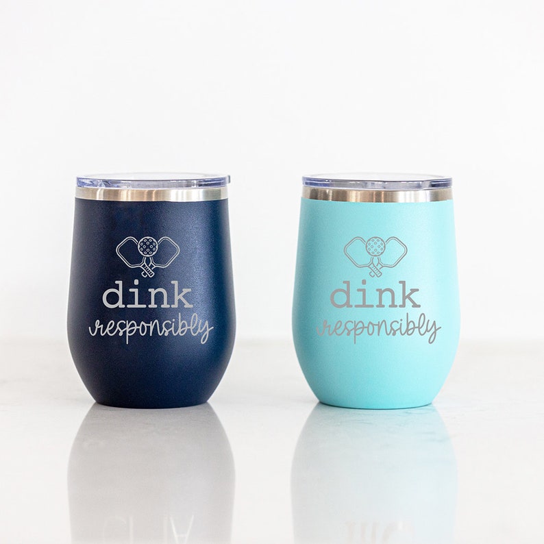 May include: Two stainless steel wine tumblers with a blue and a turquoise finish. Both tumblers feature a white silhouette of two pickleball paddles and the text "dink responsibly".