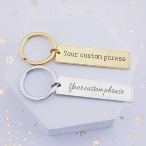May include: Two gold and silver keychains with a rectangular tag that says "Your custom phrase".