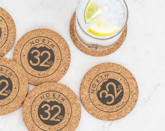 Puede incluir: Juego de seis posavasos de corcho marrón con un diseño circular negro que presenta el texto "NORTH 32ND".