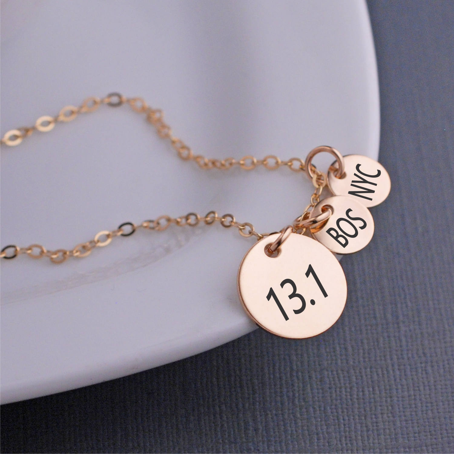 May include: Gold necklace with three round charms. The charms are engraved with "13.1", "BOS", and "NYC".