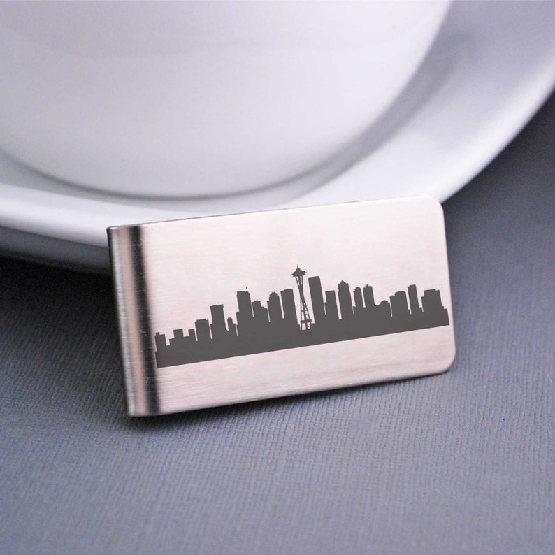 K&ouml;nnte beinhalten: Ein silberner Geldclip mit einer lasergravierten Silhouette der Skyline von Seattle, einschlie&szlig;lich des Space Needle.