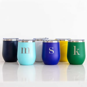 May include: Six stainless steel tumblers with different colored exteriors and a single letter engraved on each. The colors are navy blue, light blue, white, blue, yellow, and green. The letters are M, S, and K.