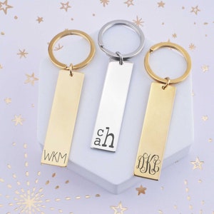 May include: Three gold and silver keychains with engraved initials. The keychains are rectangular and have a ring attached to the top. The initials are "WKM", "ch", and "DKL".