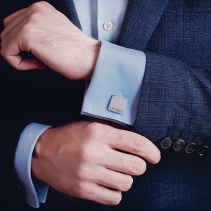 a stainless steel cufflink shown on a men's shirt sleeve.