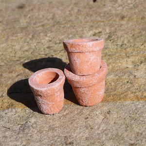 以下が含まれることがあります： テラコッタ色の小さな粘土鉢が3つ。2つの鉢が積み重ねられ、1つは別になっています。鉢はざらざらとした質感で、釉薬は塗られていません。ミニチュア植物や装飾用に適しています。