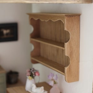 May include: A wooden shelf unit with two shelves and a scalloped edge. The shelf is made of light brown wood and is mounted on a white wall.