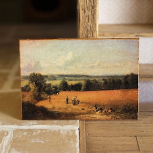 May include: A framed painting depicting a rural landscape with a field of wheat, a group of people in the distance, and a cloudy sky.