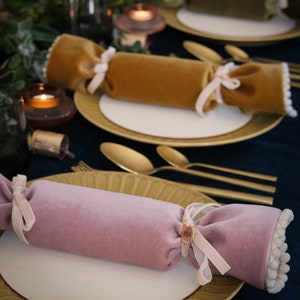 May include: Three velvet Christmas crackers with gold, green, and pink fabric. Each cracker is tied with a ribbon and has a small tag with the initials "HM".