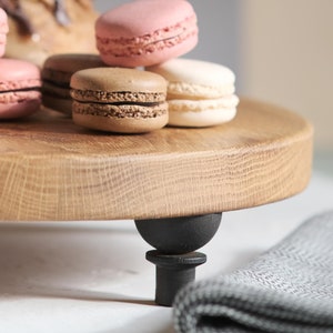 May include: A wooden serving tray with black feet, holding a stack of colorful macarons. The macarons are pink, brown, and white.