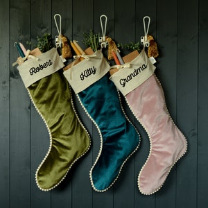 May include: Three velvet Christmas stockings with pom-pom trim and personalised names: Robert, Kitty, and Grandma.