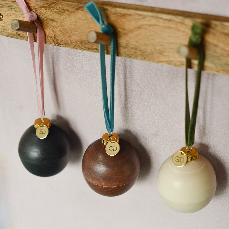 May include: Three wooden ornaments with gold tags hanging from velvet ribbon. The ornaments are black, brown, and white. The tags have the initials "ED", "CD", and "GD" on them.