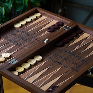 Könnte beinhalten: Ein Backgammon-Set aus Holz mit dunkelbrauner Oberfläche. Das Brett ist geöffnet und zeigt die Spielfläche mit weißen und braunen Feldern. Auf dem Brett befinden sich weiße und braune Spielsteine. Das Brett ist mit dem Text "Team Covenant 2022" und "The journey is what matters" graviert.