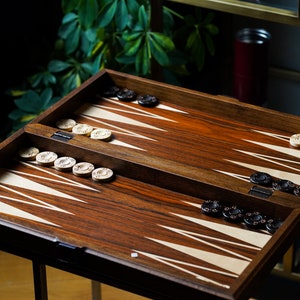 May include: A wooden backgammon board with white and black playing pieces. The board is open and the pieces are arranged in a playing formation.