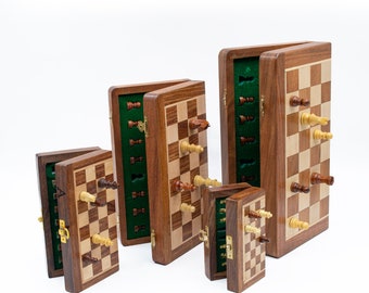 May include: A set of four wooden chess sets in various sizes, all with the pieces stored inside the board. The boards are open and the pieces are visible. The chess sets are made of dark wood with a light wood inlay.