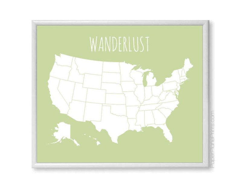 May include: A framed print featuring a map of the United States in white against a light green background. The word "WANDERLUST" is written in a handwritten style font at the top. The print is in a white frame.