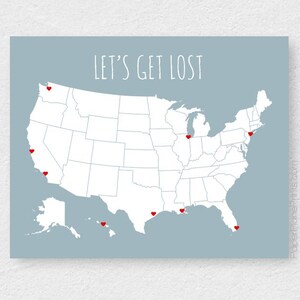 May include: A map of the United States with red heart markers on various locations. The phrase "LET'S GET LOST" is written in white script across the top of the map. The background is a light blue color.