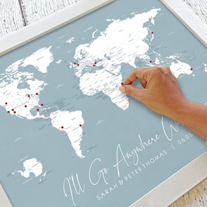 May include: A blue and white world map with red push pins marking locations. The map is framed in white and has the text "I'll Go Anywhere" with the names "Sarah & Peter Thomas" and the date "06.03".