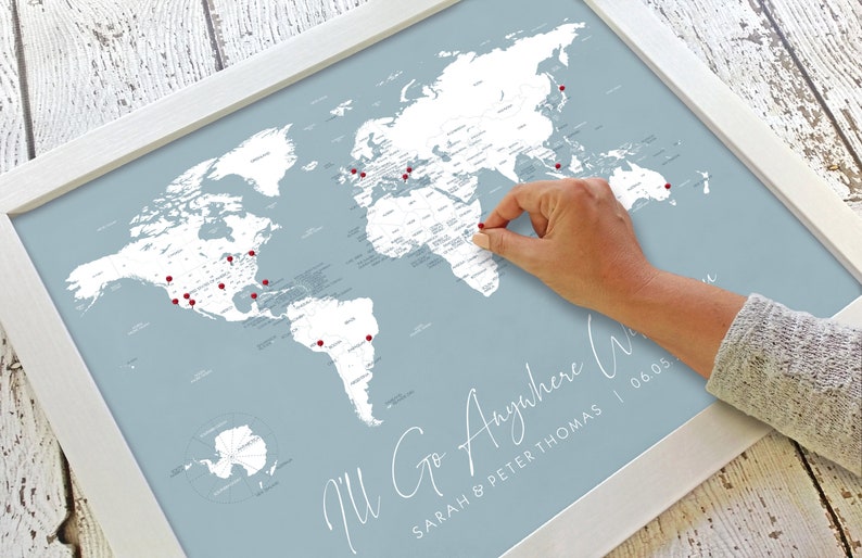 May include: A blue and white world map with red push pins marking locations. The map is framed in white and has the text "I'll Go Anywhere" with the names "Sarah & Peter Thomas" and the date "06.03".