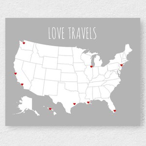 May include: A gray print featuring a white map of the United States with red heart markers. The text "LOVE TRAVELS" is displayed above the map. The print is a decorative item.