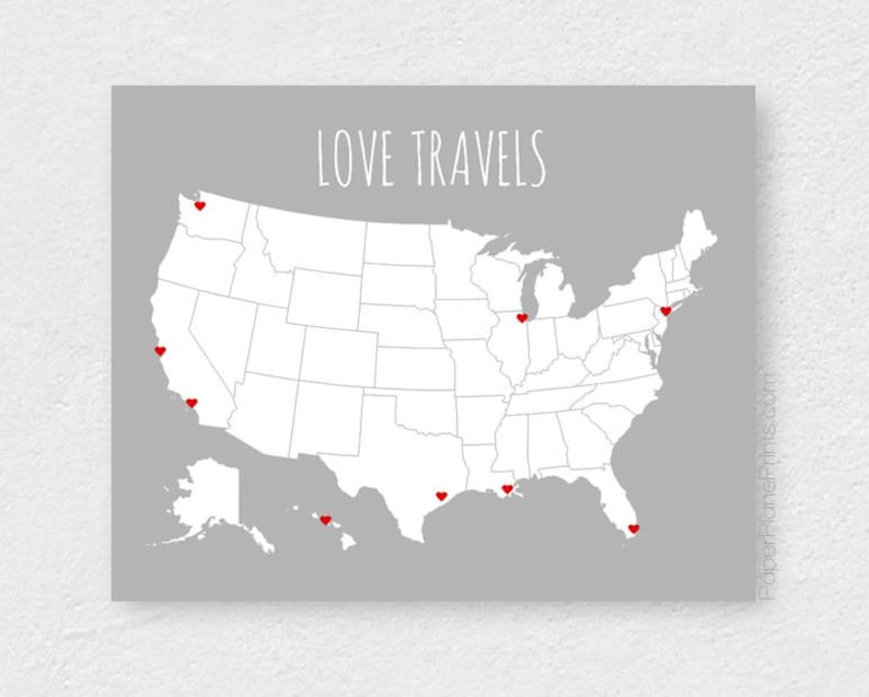 May include: A gray print featuring a white map of the United States with red heart markers. The text "LOVE TRAVELS" is displayed above the map. The print is a decorative item.