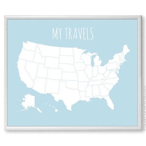 May include: A framed map of the United States with a light blue background. The map is white, showing state outlines. The words "MY TRAVELS" are in white script at the top. The frame is white.