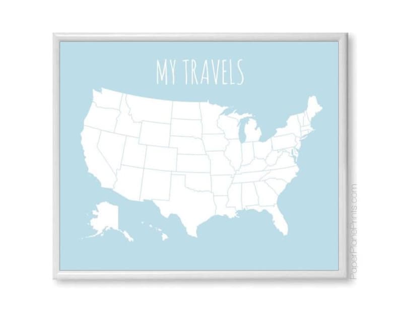May include: A framed map of the United States with a light blue background. The map is white, showing state outlines. The words "MY TRAVELS" are in white script at the top. The frame is white.