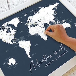 May include: A white world map with gold push pins on a dark blue background. The map is framed in white and has the text "Adventure is out" and "Logan's Travels" written below the map.