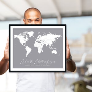May include: A framed world map with a grey background and white outlines of countries. The map is titled "And so the Adventure Begins" with the text "Sarah & Peter Thomas | 28.09.2020" below the title.