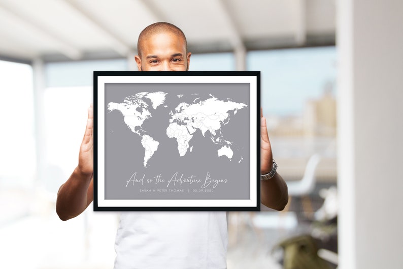 May include: A framed world map with a grey background and white outlines of countries. The map is titled "And so the Adventure Begins" with the text "Sarah & Peter Thomas | 28.09.2020" below the title.