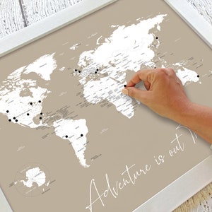Beautiful decorative couples world push pin map for marking travels and places visited. With script cursive Adventure is out There travel quote title. Shown in neutral taupe beige and customizable to other colors and personalized names and date.