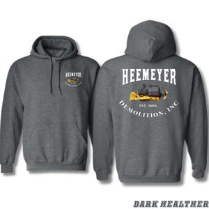May include: Dark heather grey hooded sweatshirt with a white graphic of a yellow bulldozer and the text "Heemeyer Demolition, Inc. Est. 2004".