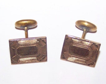 May include: A pair of gold-toned cufflinks with a rectangular design. The cufflinks have a detailed engraved pattern.