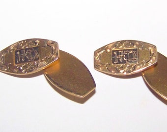 May include: A pair of gold cufflinks with an engraved design. The cufflinks feature a rectangular shape with the initials "H.D." in the center. The initials are surrounded by a floral design.